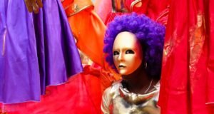 Disfraces identidad y tradición en eventos contemporáneos Persona eligiendo disfraz en tienda de Alcalá de Guadaíra con trajes coloridos y accesorios festivos.