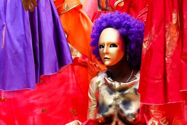VivaFiesta Persona eligiendo disfraz en tienda de Alcalá de Guadaíra con trajes coloridos y accesorios festivos.